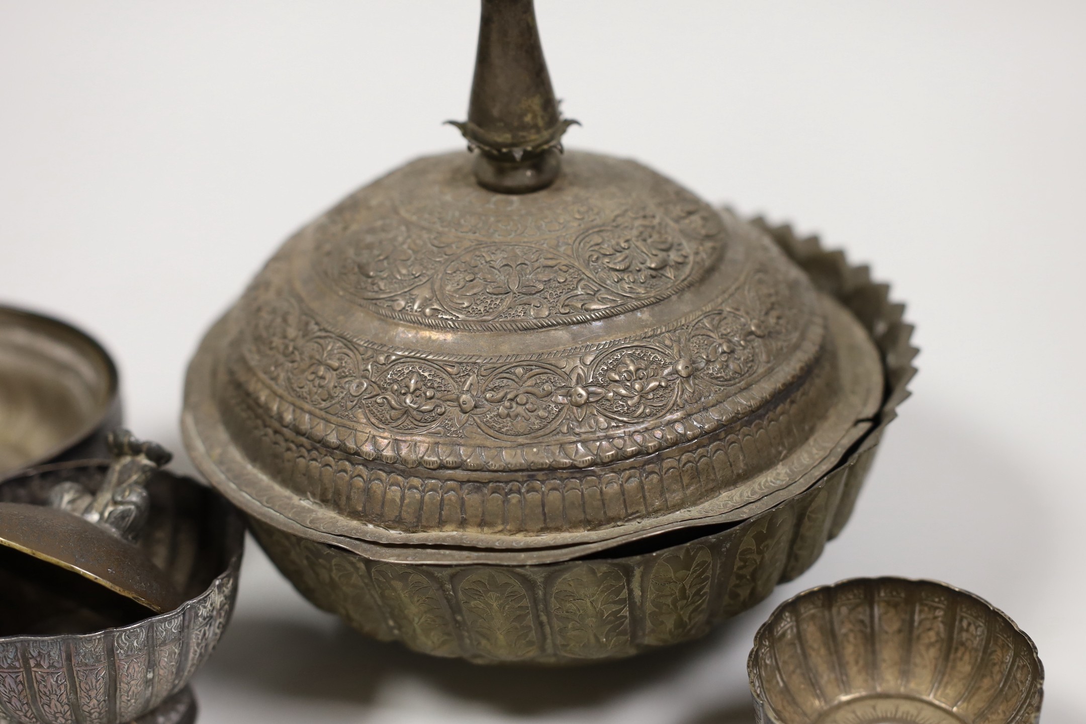 A Malay Straits pedestal bowl and cover or 'Batil Ber Tutop' (a.f.), three Malay Straits white metal betel nut cups and two similar small bowls, all with embossed floral or foliate designs (one cup with green enamelled d